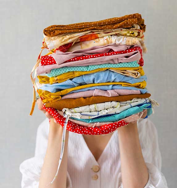 woman-s-hands-holding-large-stack-of-colorful-laun-2022-11-14-00-21-55-utc